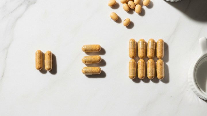 Nattokinase capsules arranged in three dosage groups on marble surface showing different daily dose options